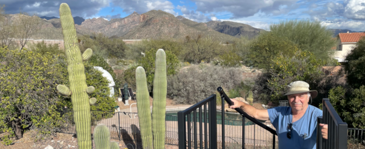 Prof. David G. Iadevaia outdoors among saguaro cacti with mountains and an observatory dome in the background